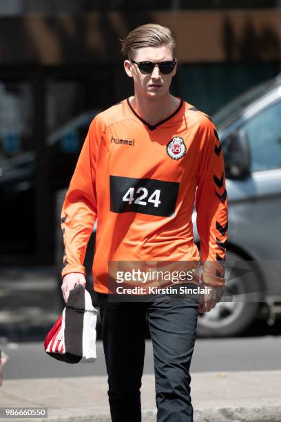 Guest wears a Hummel top, Ray ban sunglasses, Acne bag during London Fashion Week Men's on June 9, 2018 in London, England.