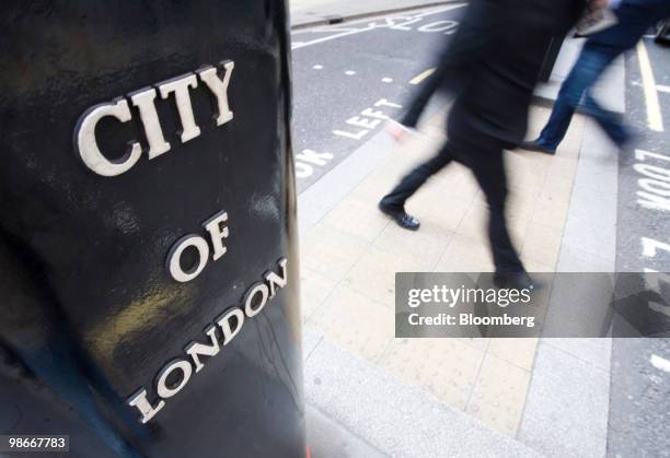 Pedestrians pass a pedestal supporting a statue of a Griffin which carries the coat of arms of the City of London, in London, U.K., on Friday, April...