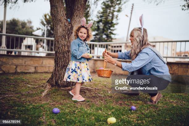 girl looking for eggs during easter egg hunt with grandmother - easter egg hunt outside stock pictures, royalty-free photos & images