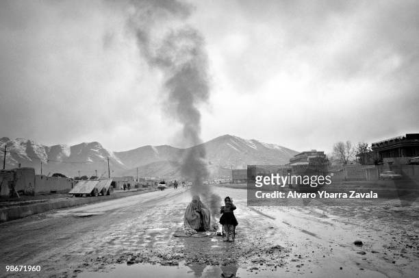 Woman wearing a burqa, with a young girl, sit in the middle of a muddy road in front of a bonfire. Over 3.5 million Afghan refugees have returned to...