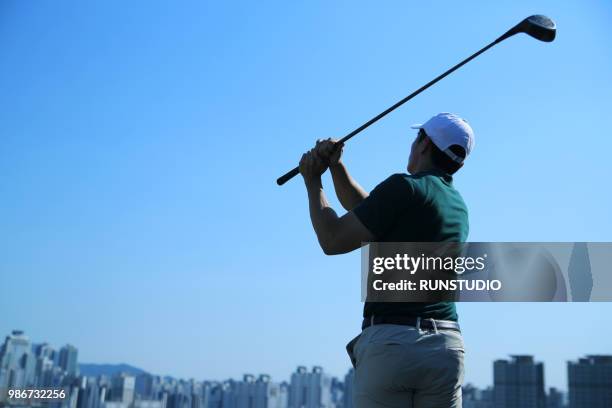 man swinging golf club against clear sky - adventure club stockfoto's en -beelden
