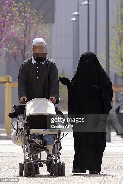 Woman wearing a niqab, the islamic full veil, walks with a man pushing a stroller in a street of Venissieux near Lyon, eastern France, on April 22,...