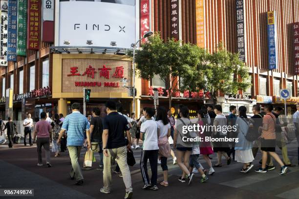 Pedestrians and shoppers cross a road in front of the Wangfu Mall on Wangfujing Street in Beijing, China, on Wednesday, June 27, 2018. Consumer...