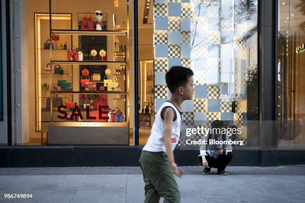 Pedestrian uses a mobile phone outside a Furla SpA store on Wangfujing Street in Beijing, China, on Wednesday, June 27, 2018. Consumer sentiment in...