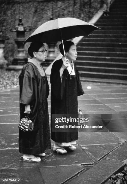 Two Japanese women wearing traditional kimonos and geta stand in front of a Shinto shrine in Nikko, Japan.