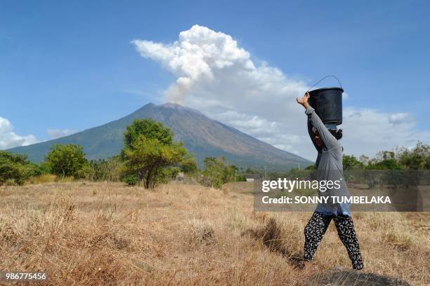 Balinese woman carries a bucket of water as Mount Agung volcano erupts at the Kubu sub-district in Karangasem Regency on Indonesia's resort island of...