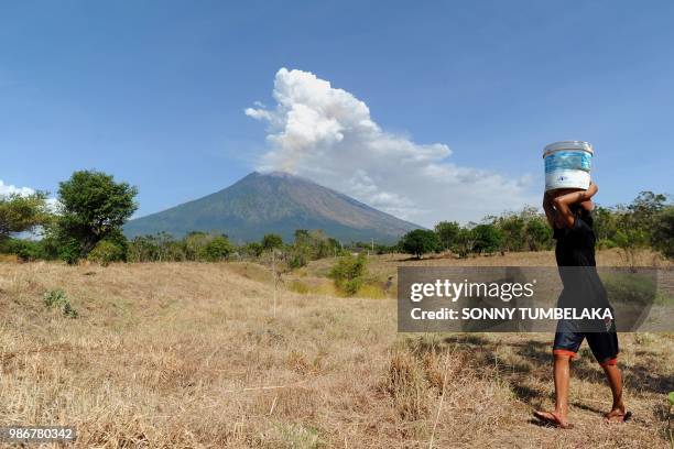 Balinese girl carries a bucket of water on her head as Mount Agung volcano erupts at the Kubu sub-district in Karangasem Regency on Indonesia's...