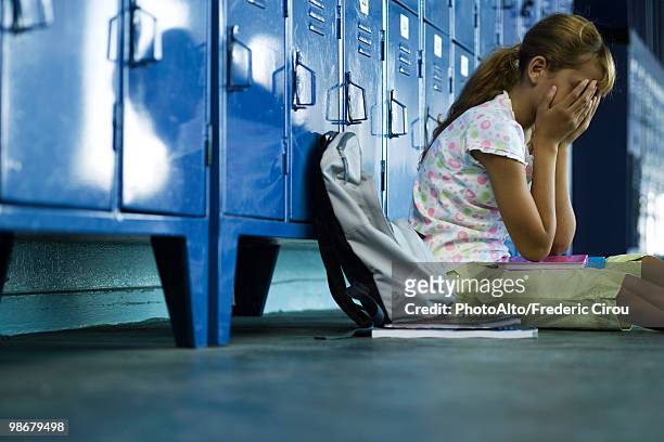 female junior high student sitting on hall floor near lockers, upset and covering face with hands - junior high student stockfoto's en -beelden