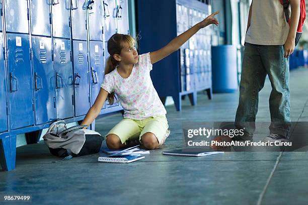 female junior high student sitting on floor pointing angrily up at boy standing over her - exigir fotografías e imágenes de stock
