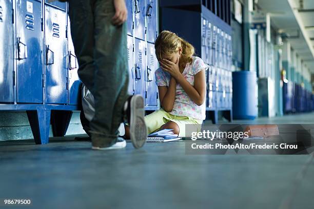 female junior high student sitting on floor holding head in hands, boy standing smugly nearby - arrogant stock-fotos und bilder