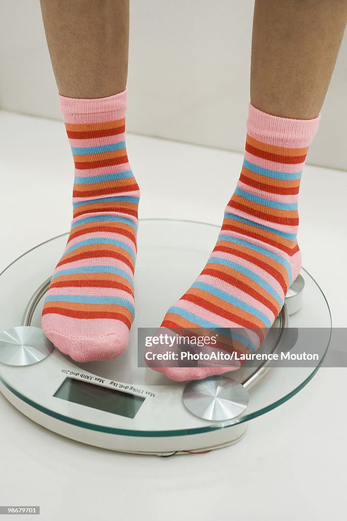 Girl weighing self on bathroom scale, cropped