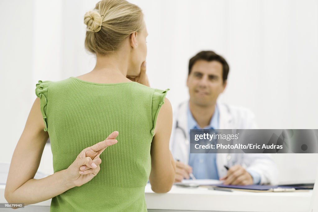 Female patient with hand behind back crossing fingers, speaking with doctor