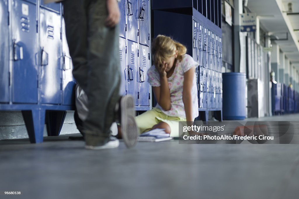 Junior high student sitting on floor crying, boy standing by watching