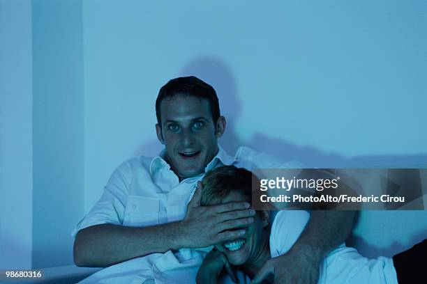 couple watching tv together, man covering woman's eyes with his hand - woman watching horror movie stock pictures, royalty-free photos & images