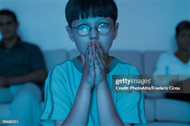 boy watching tv with hands clasped over mouth, parents sitting in background - 見つめる ストックフォトと画像