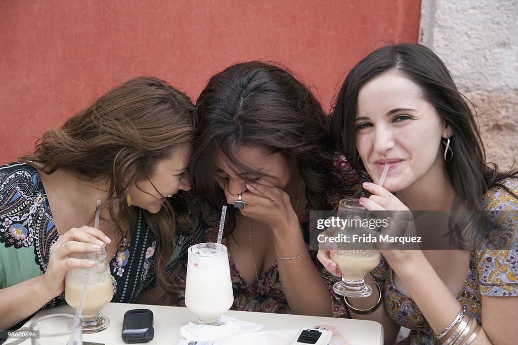 Hispanic women laughing and drinking at cafe