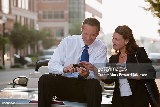 caucasian businessman sitting on car text messaging with co-worker - co op city stock pictures, royalty-free photos & images