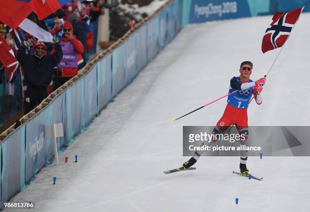Johannes Hoesflot Klaebo of Norway carries his country's flag as he crosses the finish line of the men's 4x10km Cross Country Skiing Relay race...