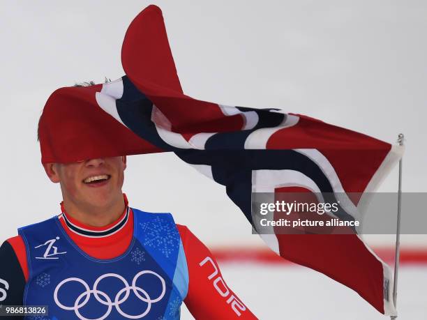 Johannes Hoesflot Klaebo of Norway carries his country's flag after crossing the finish line of the men's 4x10km Cross Country Skiing Relay race...