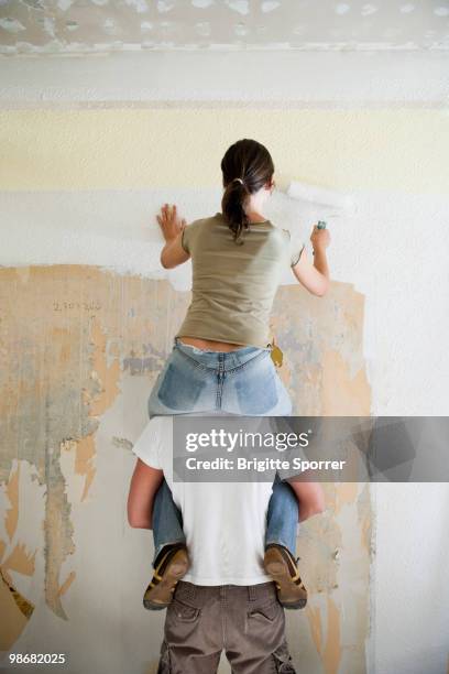 young couple painting wall - woman sitting on shoulders stock pictures, royalty-free photos & images