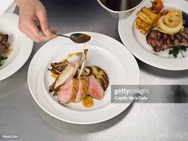 a hand drizzling gravy on some lamb - food plating stock-fotos und bilder