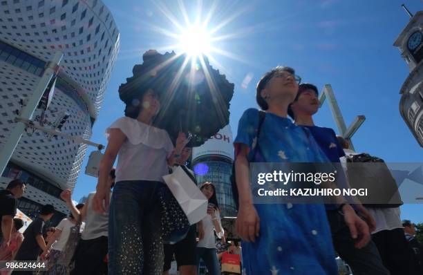 People walk along a crossing on a sunny day in Tokyo's Ginza shopping district on June 29, 2018. - The Japan Meteorological Agency announced on June...
