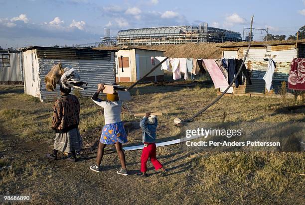 Family carries firewood in a poor shantytown in front of the newly constructed Orlando Stadium on June 21, 2008 in Soweto, South Africa. Many people...