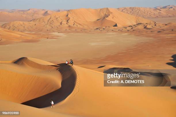 sultanate of oman, dhofar, rub al khali desert, called the empty quarter, the largest sand area in the world,border of yemen and saoudi arabia, a group of tourists is standing on the top of a high sand dune in the middle of a ochre sand desert - dhofar stock pictures, royalty-free photos & images