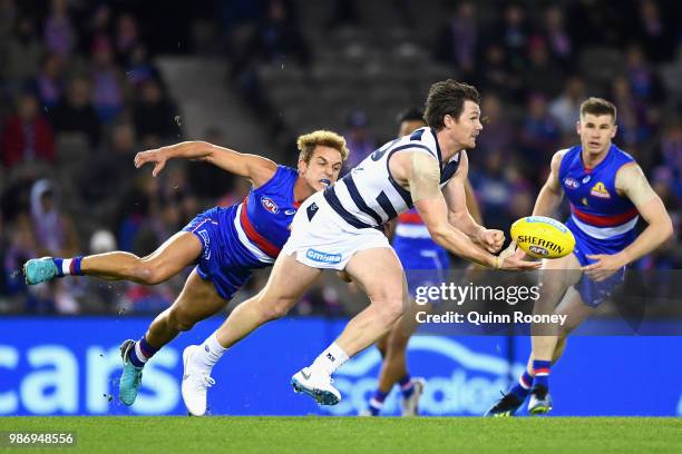 Patrick Dangerfield of the Cats handballs whilst being tackled by Mitch Wallis of the Bulldogs during the round 15 AFL match between the Western...
