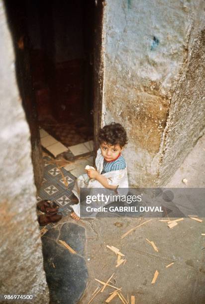 Un enfant portant le vêtement des "nouveaux baptisés" est assis près dans le porche d'une maison, en octobre 1971, dans une rue de la Casbah d'Alger....