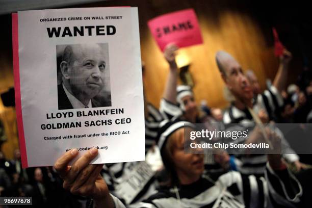 Demonstrators from Code Pink for Peace hold photographs of Lloyd Blankfein, chairman and CEO of The Goldman Sachs Group, and demand he be jailed with...