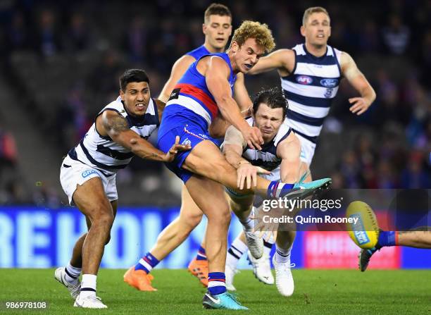 Mitch Wallis of the Bulldogs kicks whilst being tackled by Tim Kelly and Patrick Dangerfield of the Cats during the round 15 AFL match between the...