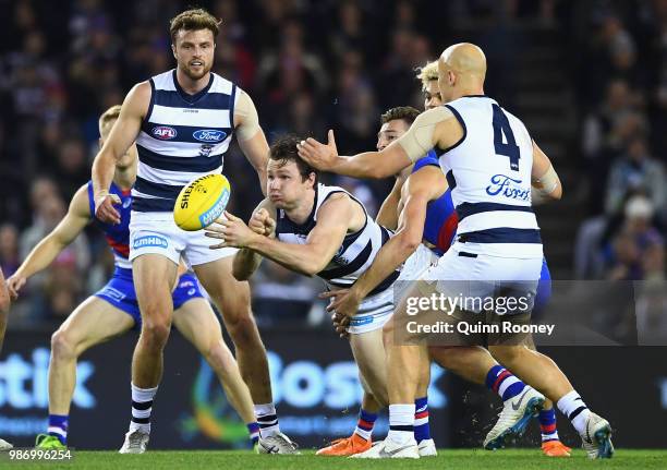 Patrick Dangerfield of the Cats handballs whilst being tackled during the round 15 AFL match between the Western Bulldogs and the Geelong Cats at...