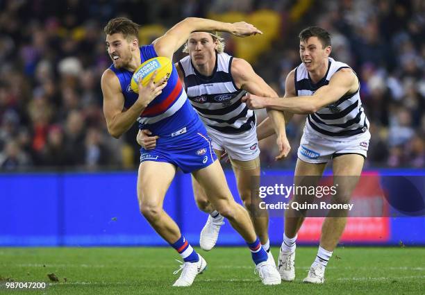 Marcus Bontempelli of the Bulldogs breaks free of a tackle by Mark Blicavs and Jack Henry of the Cats during the round 15 AFL match between the...