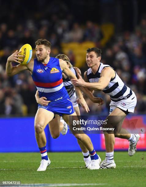 Marcus Bontempelli of the Bulldogs breaks free of a tackle by Mark Blicavs and Jack Henry of the Cats during the round 15 AFL match between the...