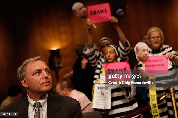 Demonstrators from Code Pink for Peace hold signs behind David Viniar, executive vice president and Chief Financial Officer at the Goldman Sachs...