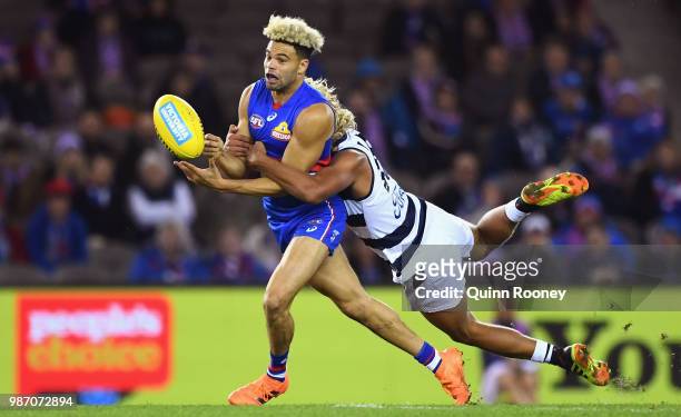 Jason Johannisen of the Bulldogs handballs whilst being tackled by Quinton Narkle of the Cats during the round 15 AFL match between the Western...