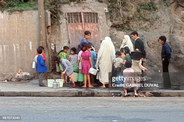 Trois femmes voilées et une quinzaine de jeunes remplissent, en octobre 1971, des sceaux en plastique à un point de ravitaillement en eau dans une...