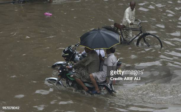 Pakistani motorcyclists ride through a flooded street after heavy rains in Lahore on June 29, 2018.