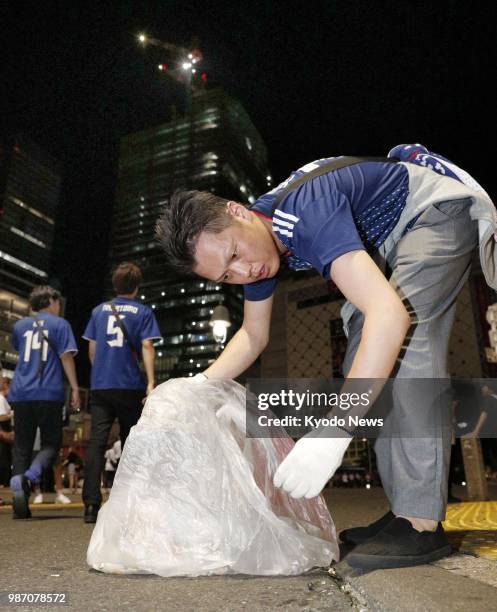 Man wearing a Japan national football team's shirt collects litter in Tokyo's Shibuya in the early hours of June 29 after football fans crowded the...