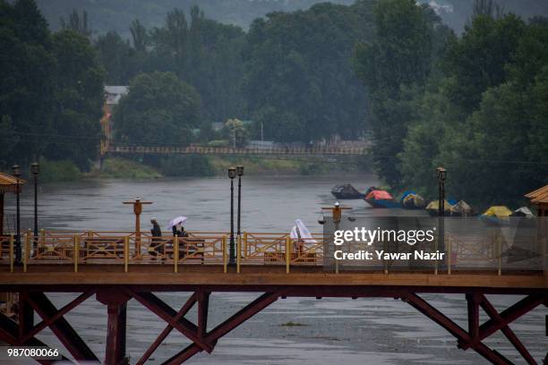 People walk on a bridge overflowing Jehlum River amid rains on June 29, 2018 in Srinagar, the summer capital of Indian administered Kashmir, India. A...