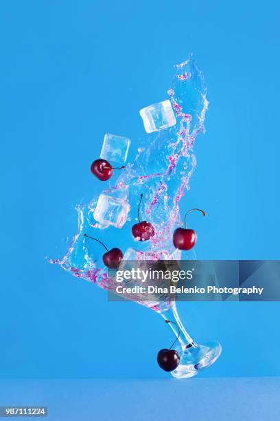 martini glass with ice cubes and cherries on a bright blue background with copy space. high-speed photography with dynamic splash. refreshing cocktail concept - khabarovsk krai stockfoto's en -beelden