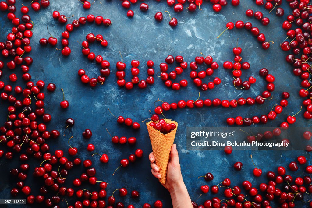 Fresh cherries in a waffle ice cream cone forming a word Sweet on a stone background with copy space. Food typography or food lettering concept with ripe berries