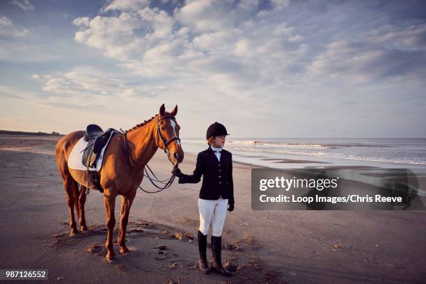 a young woman standing with her horse on the beach - breeches stock-fotos und bilder