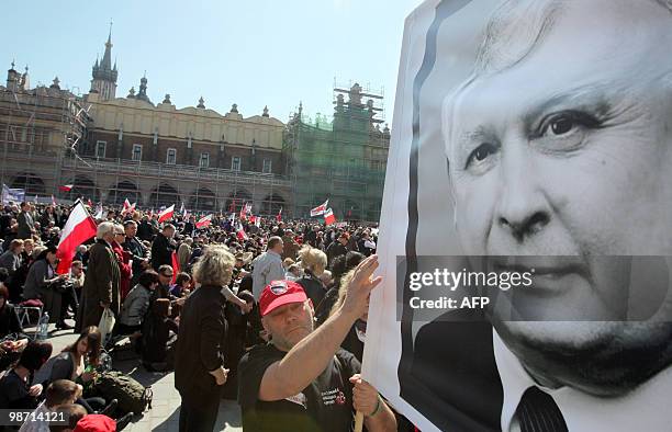 Man holds a giant protrait of late Polish President Lech Kaczynski as people gather on Krakow's market square in front of the Basilica of Our Lady...