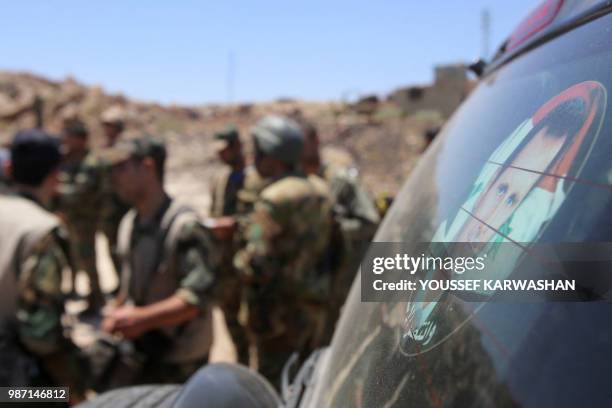 Syrian government forces talk next to a sticker representing the Syrian president Bachar al-Assad during a government guided tour in the village of...