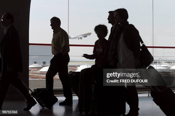 Passengers walk with their luggages at Roissy-Charles-de-Gaulle airport as a plane takes off on April 21, 2010 in Roissy-en-France, northern Paris....