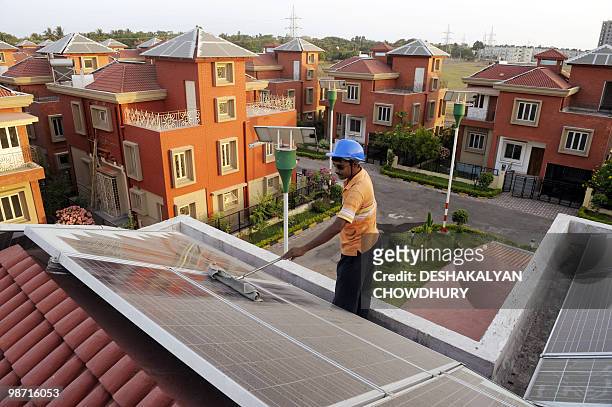 An Indian worker cleans solar panels fitted onto the roof of a residential house in Rabirashmi Abasan, a solar housing complex at Rajarhat close to...