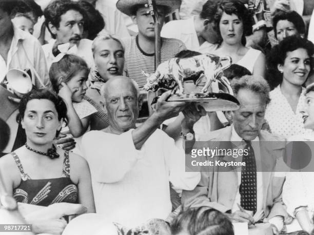 Spanish-born artist Pablo Picasso holds up a statuette of a fighting bull, presented to him by toreadors in appreciation of his art, in the stands at...