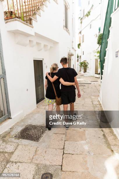 rear view of mother and son walking in whitewashed alley - cisternino stock-fotos und bilder